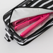 A black and white striped zippered travel pouch shown open, revealing a bright pink hair straightener and matching pink cord inside on a light gray background.