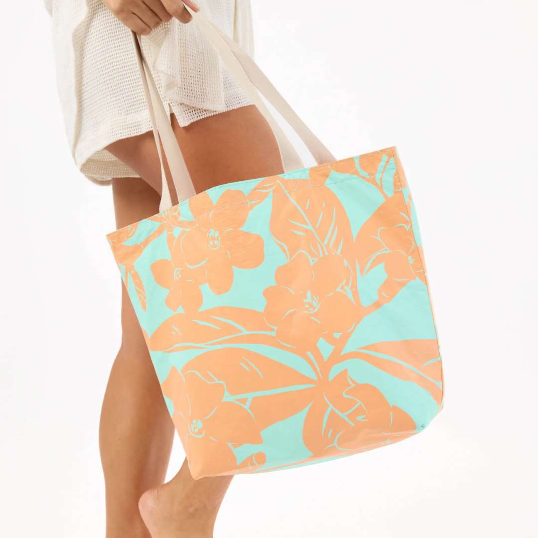 Person holding a floral tote bag with orange flowers on a light blue background