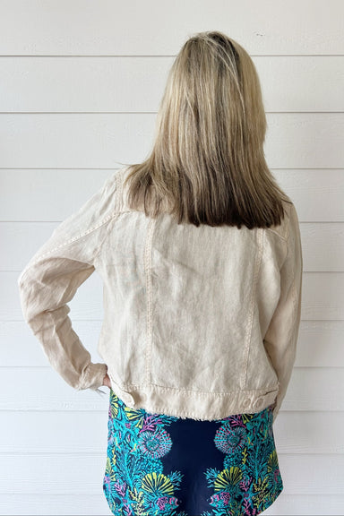 A woman shown from behind wearing a light beige linen jacket and a colorful floral print skirt, standing against a white shiplap wall.