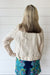 A woman shown from behind wearing a light beige linen jacket and a colorful floral print skirt, standing against a white shiplap wall.