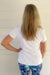 A woman viewed from behind wearing a plain white short-sleeve t-shirt and blue patterned leggings, standing against a white paneled wall.