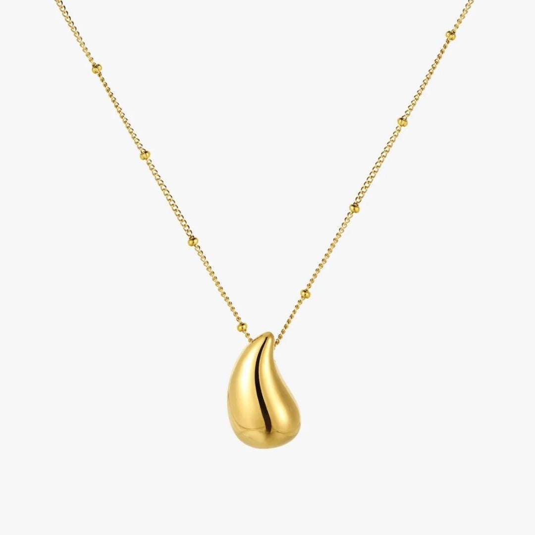 A gold necklace featuring a smooth, teardrop-shaped pendant with a polished finish and a delicate beaded chain, shown against a plain light gray background.
