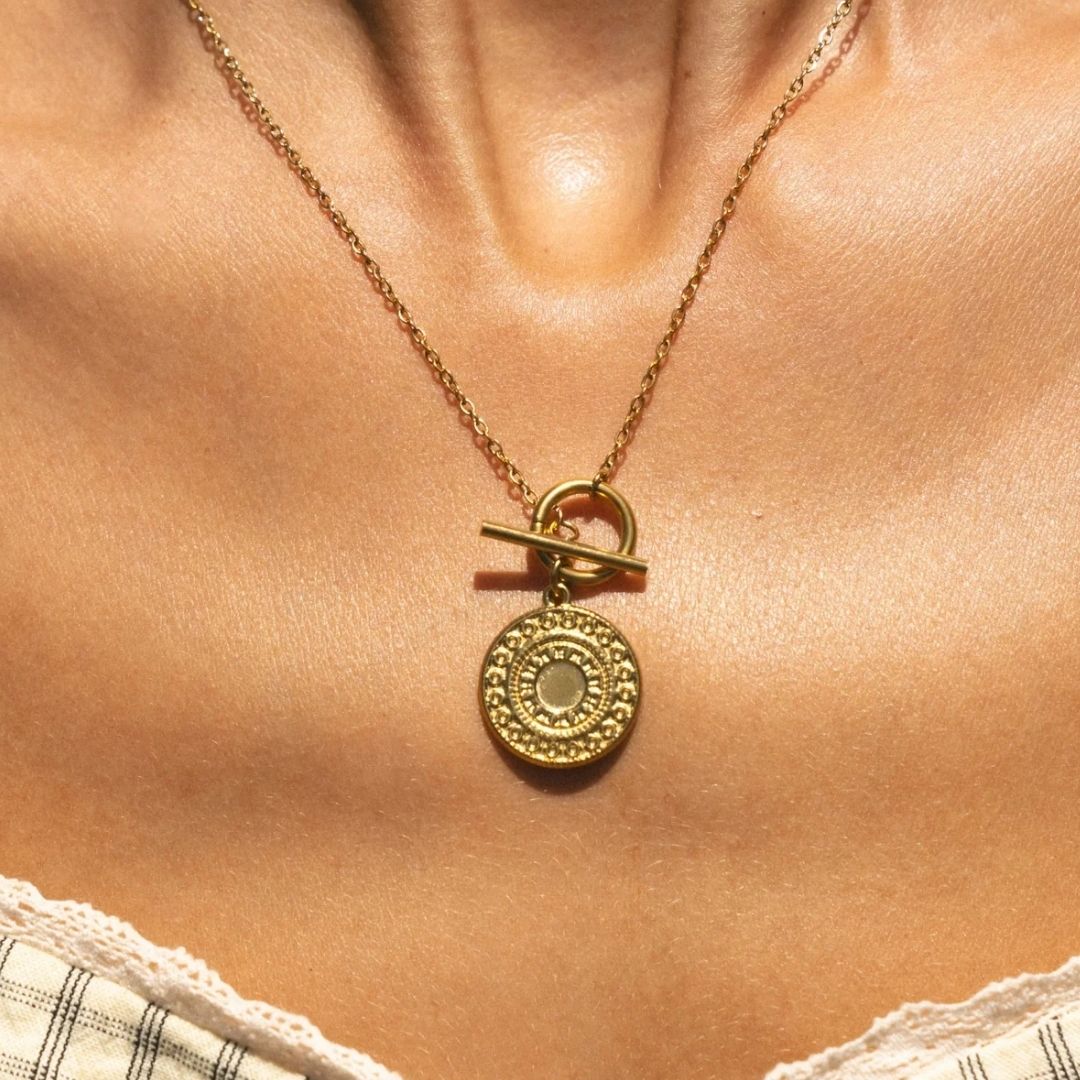 A gold necklace with a round medallion pendant and toggle clasp, shown worn on a model's neck.