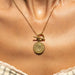 A gold necklace with a round medallion pendant and toggle clasp, shown worn on a model's neck.