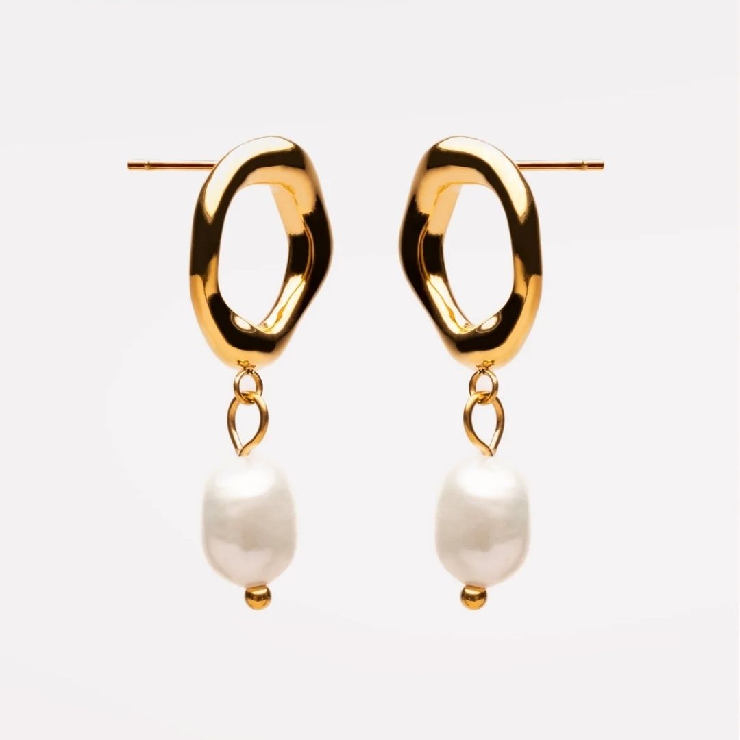 A pair of gold dangle earrings with abstract wavy oval hoops and hanging baroque-style white pearls, shown against a plain light gray background.