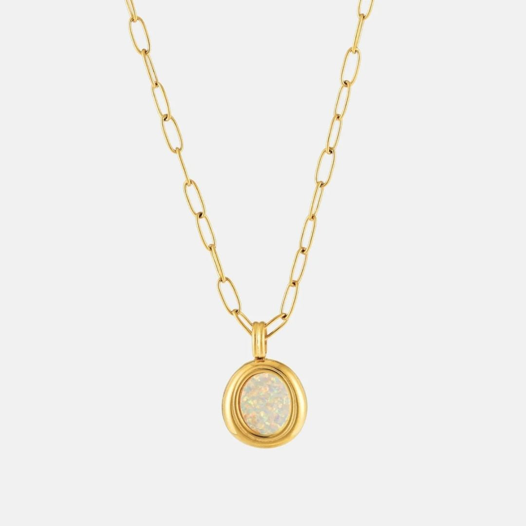A gold paperclip chain necklace with a round bezel-set opal pendant, shown against a light gray background.