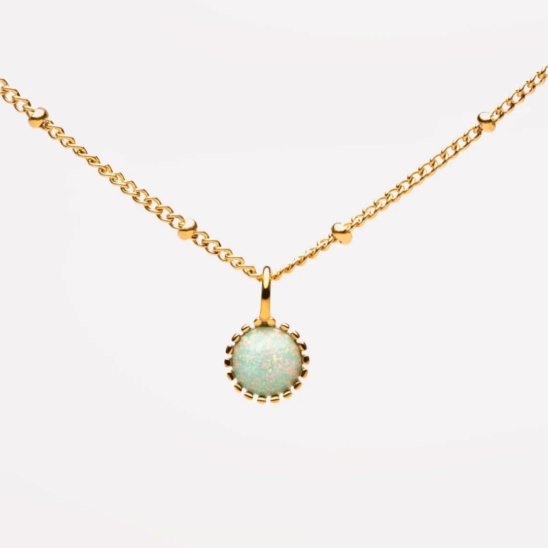 A gold chain necklace with a round bezel-set pendant featuring a light blue-green opal-like stone with subtle pink flashes, set against a plain white background.