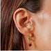 A close-up of a person's ear wearing a small gold hoop earring with a dangling polished brown stone.