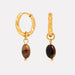 Gold hoop earrings with brown beads on a light gray background