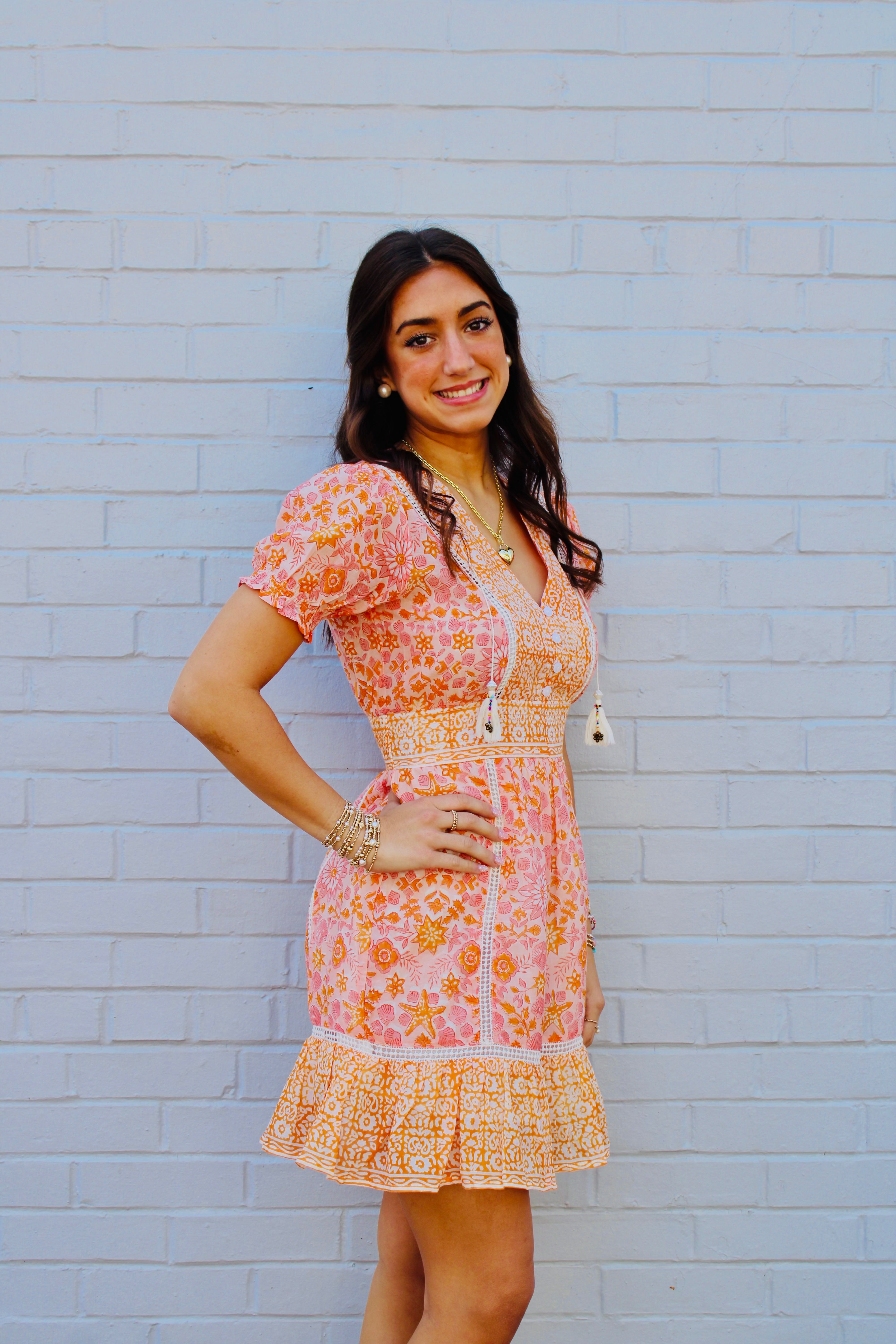 Woman wearing a floral dress standing against a light blue brick wall