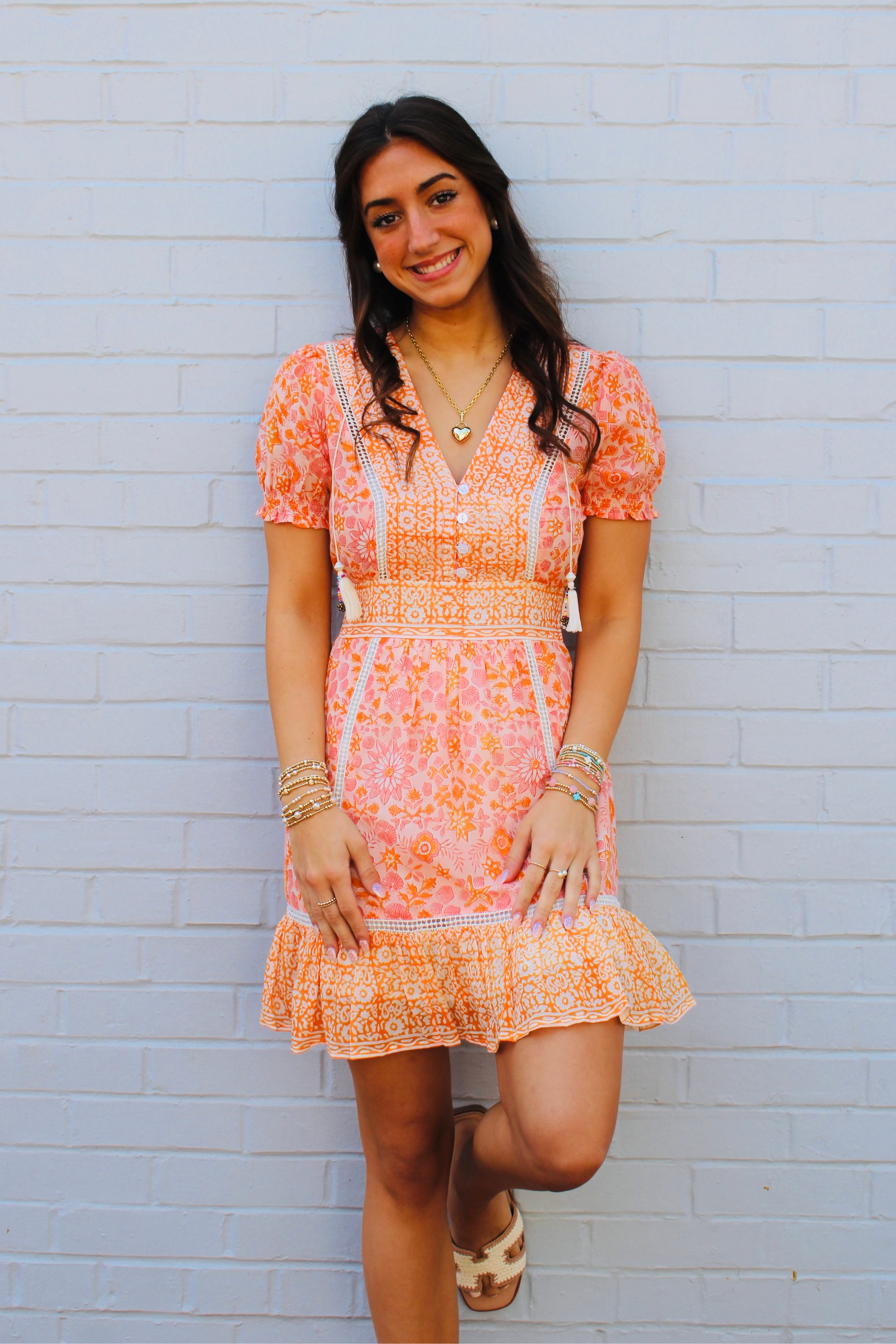 Woman wearing a pink floral dress against a light blue brick wall