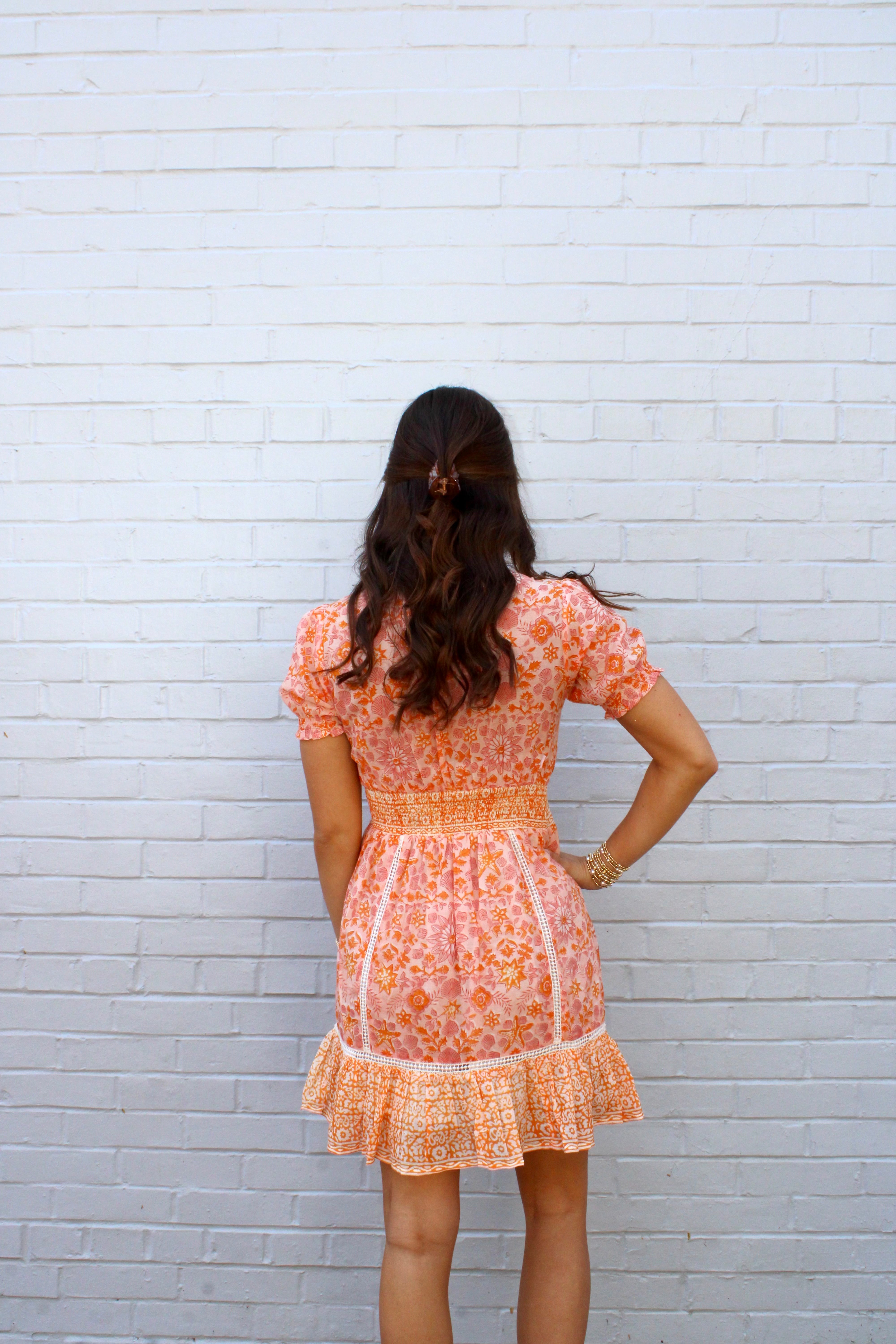 Woman wearing a floral dress against a white brick wall