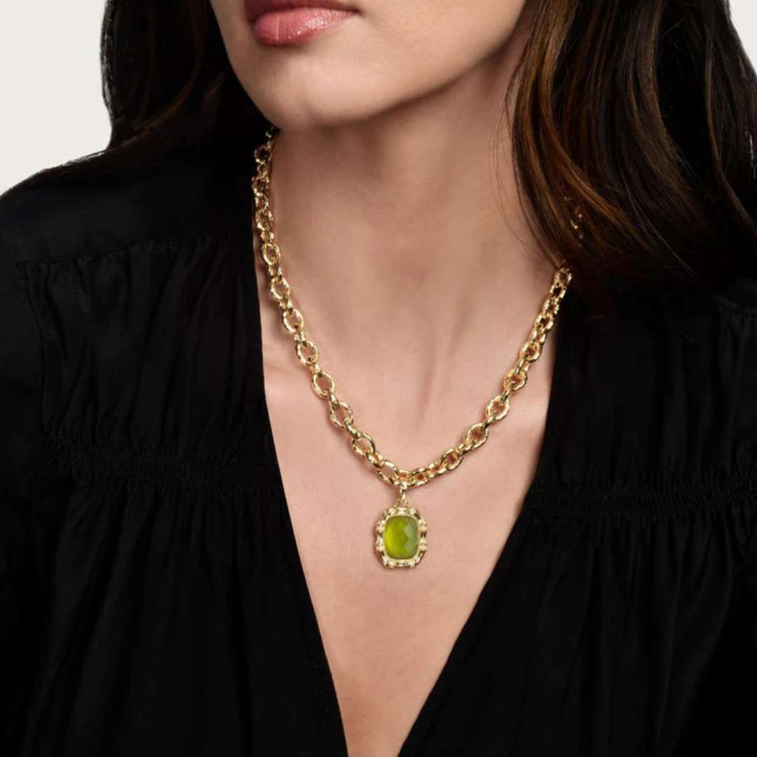 Gold necklace with a green pendant worn by a person in a black top.