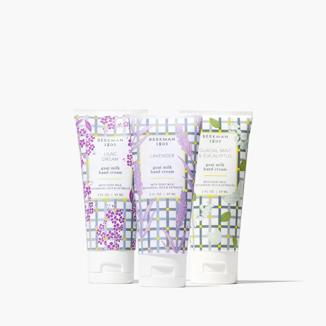 Three Beekman 1803 goat milk hand cream tubes in lilac, lavender, and eucalyptus scents, arranged side-by-side on a clean white background.