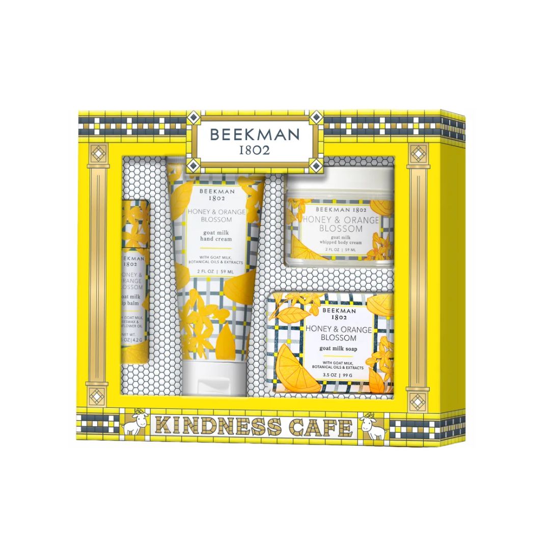 Beekman 1802 Kindness Cafe gift set containing four bath and body products: hand cream, lotion, shower gel, and soap, presented in a yellow and white patterned box.