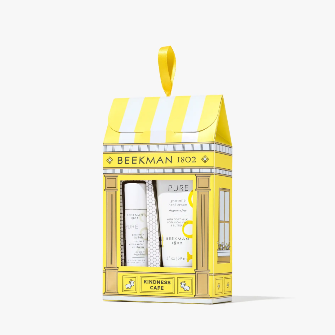 A gift set in a yellow and white storefront box labeled 'BEEKMAN 1802' and 'KINDNESS CAFE,' containing two white skincare items, shown on a clean white background.