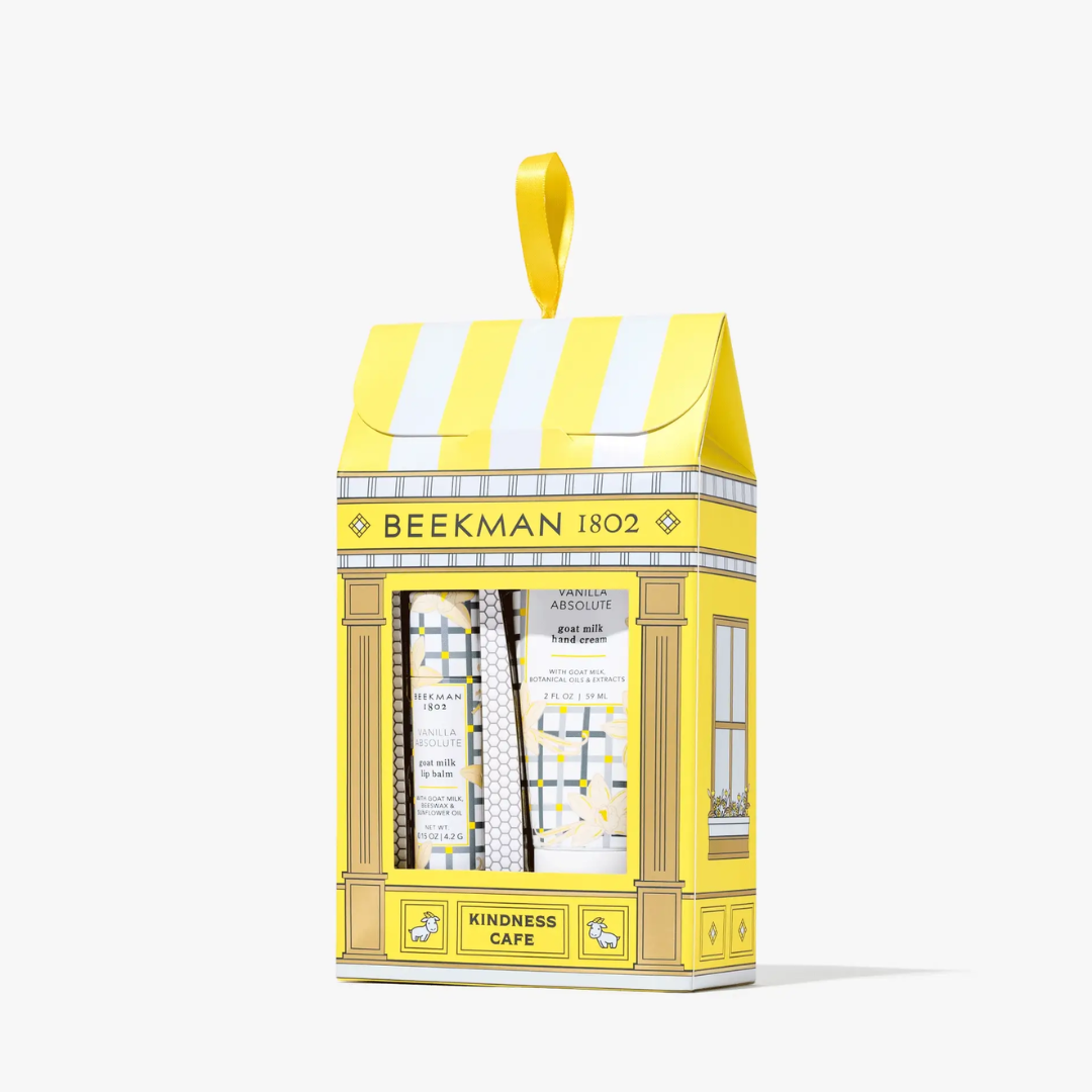 A yellow and white striped gift box shaped like a cafe storefront, with a hanging loop at the top. The box is labeled 'BEEKMAN 1802' and 'KINDNESS CAFE' and has a clear window showing rolled paper goods inside.