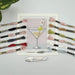 Cross-stitch pattern with a martini glass design, embroidery threads, and a scissor on a light gray background.
