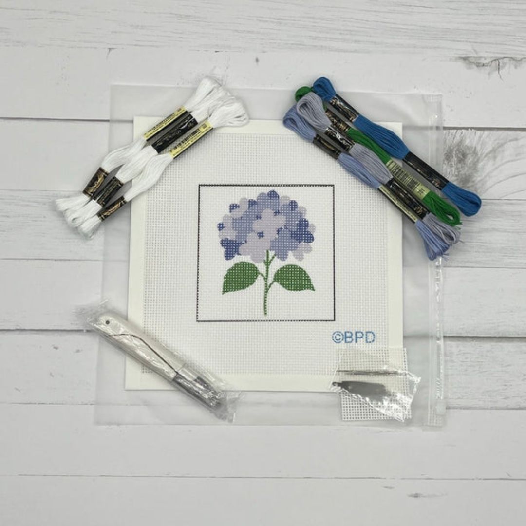 Cross-stitch kit with a completed flower design, threads, and tools on a wooden surface.