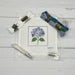Cross-stitch kit with a completed flower design, threads, and tools on a wooden surface.