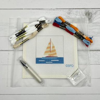 Cross-stitch kit with sailboat design, threads, and tools on a wooden surface