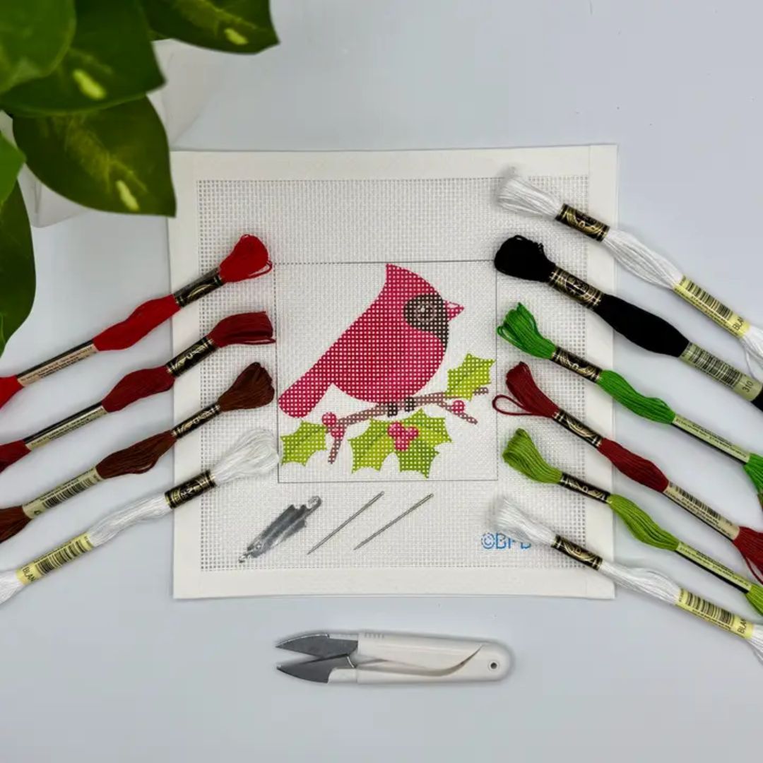 Cross-stitch kit with a red bird design, threads, and tools on a light gray background.