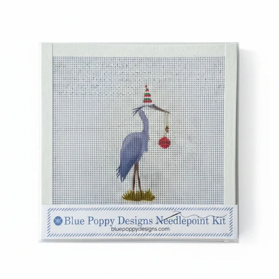 Blue Poppy Designs Needlepoint Kit featuring a blue heron holding a red ornament under a striped party hat, on a white background.