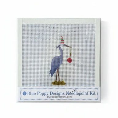 Blue Poppy Designs Needlepoint Kit featuring a blue heron holding a red ornament under a striped party hat, on a white background.