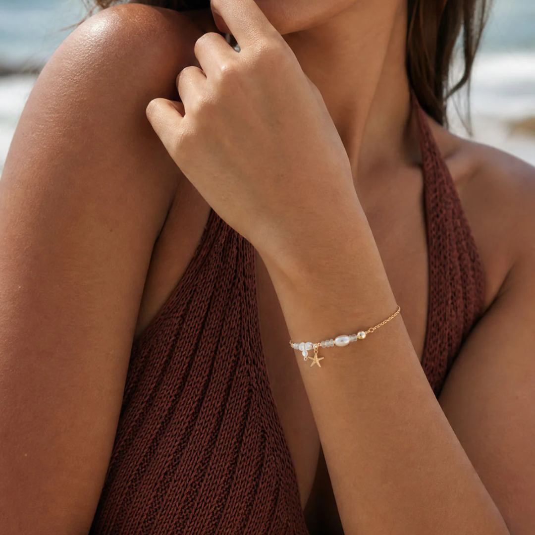 Woman wearing a gold bracelet with a star design on a beach.