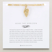 Gold bracelet with a pendant on a card featuring text and branding.