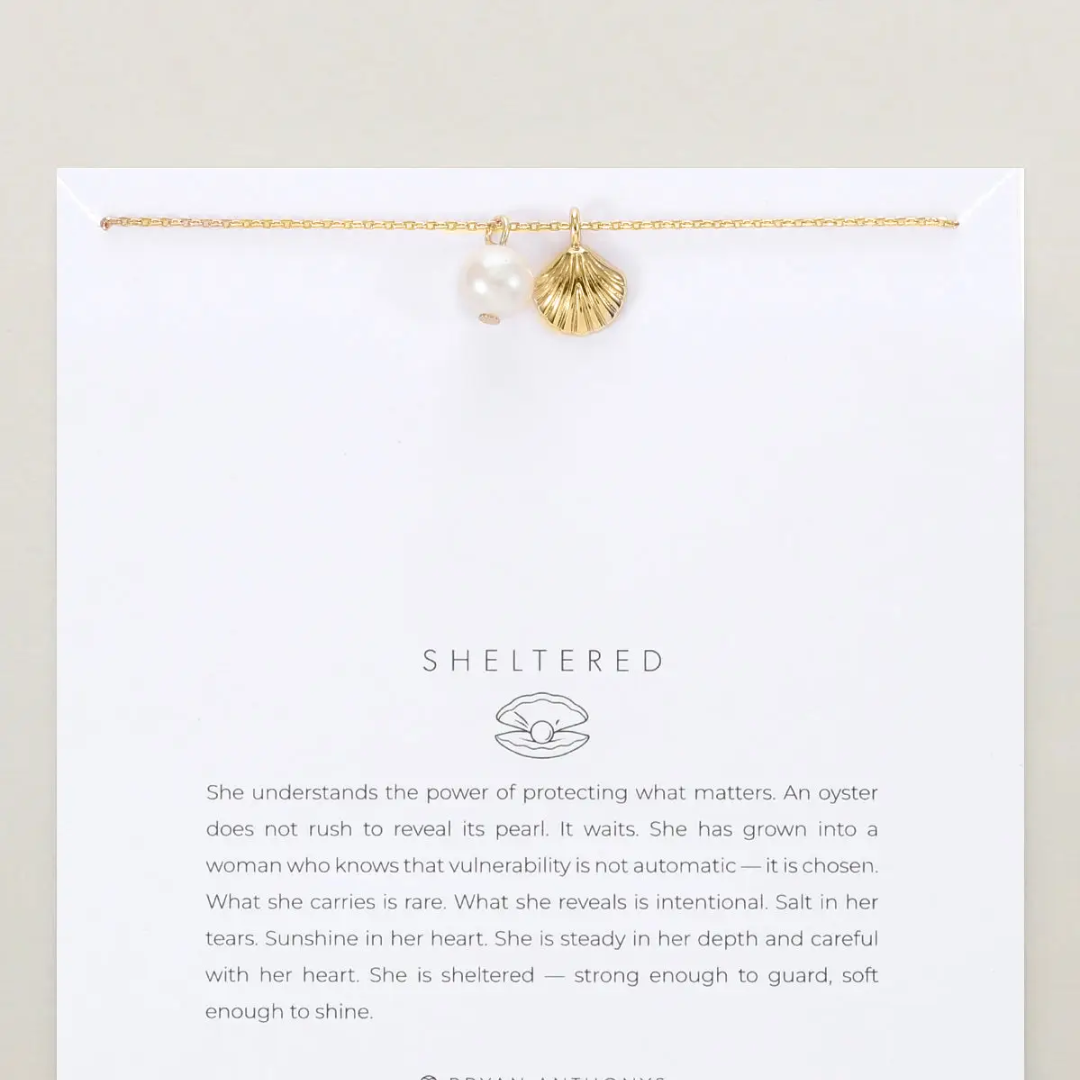 Gold bracelet with pearls on a white card featuring 'Sheltered' brand text.