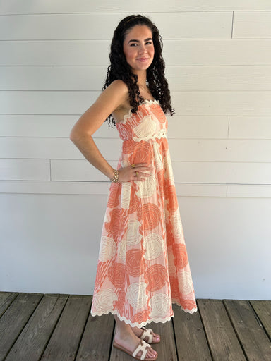 Woman wearing a seashell patterned dress standing on a wooden deck with a white wall background