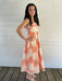 Woman wearing a seashell patterned dress standing on a wooden deck with a white wall background