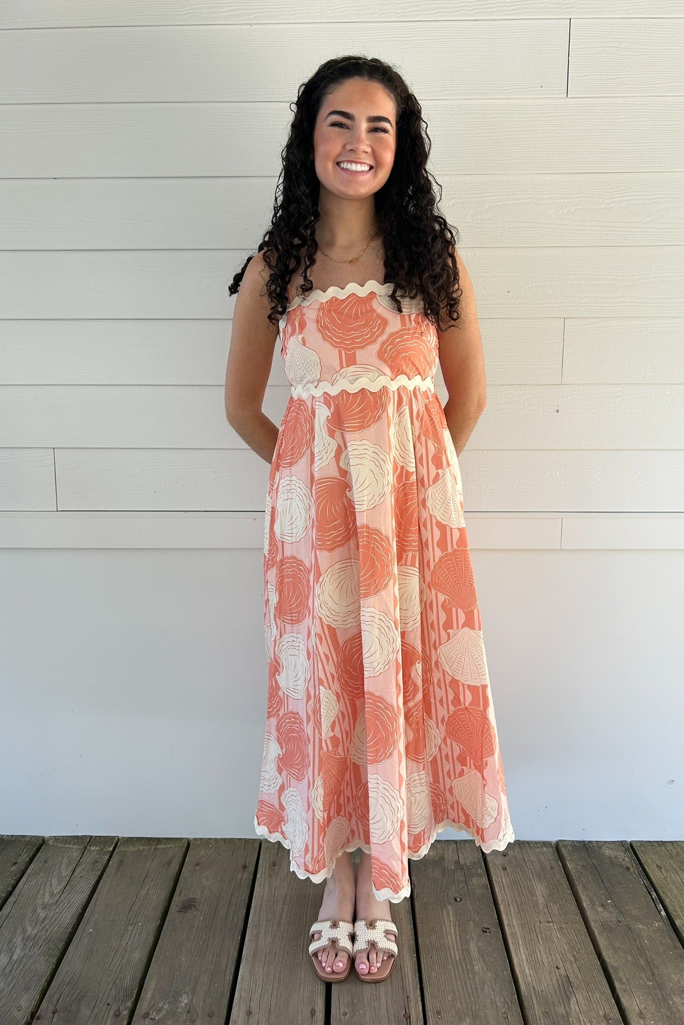 Woman wearing a shell dress standing on a wooden deck with a white wall background