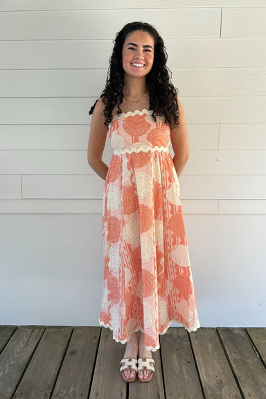 Woman wearing a shell dress standing on a wooden deck with a white wall background