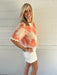 Woman wearing a floral blouse and white skirt against a light wooden panel background
