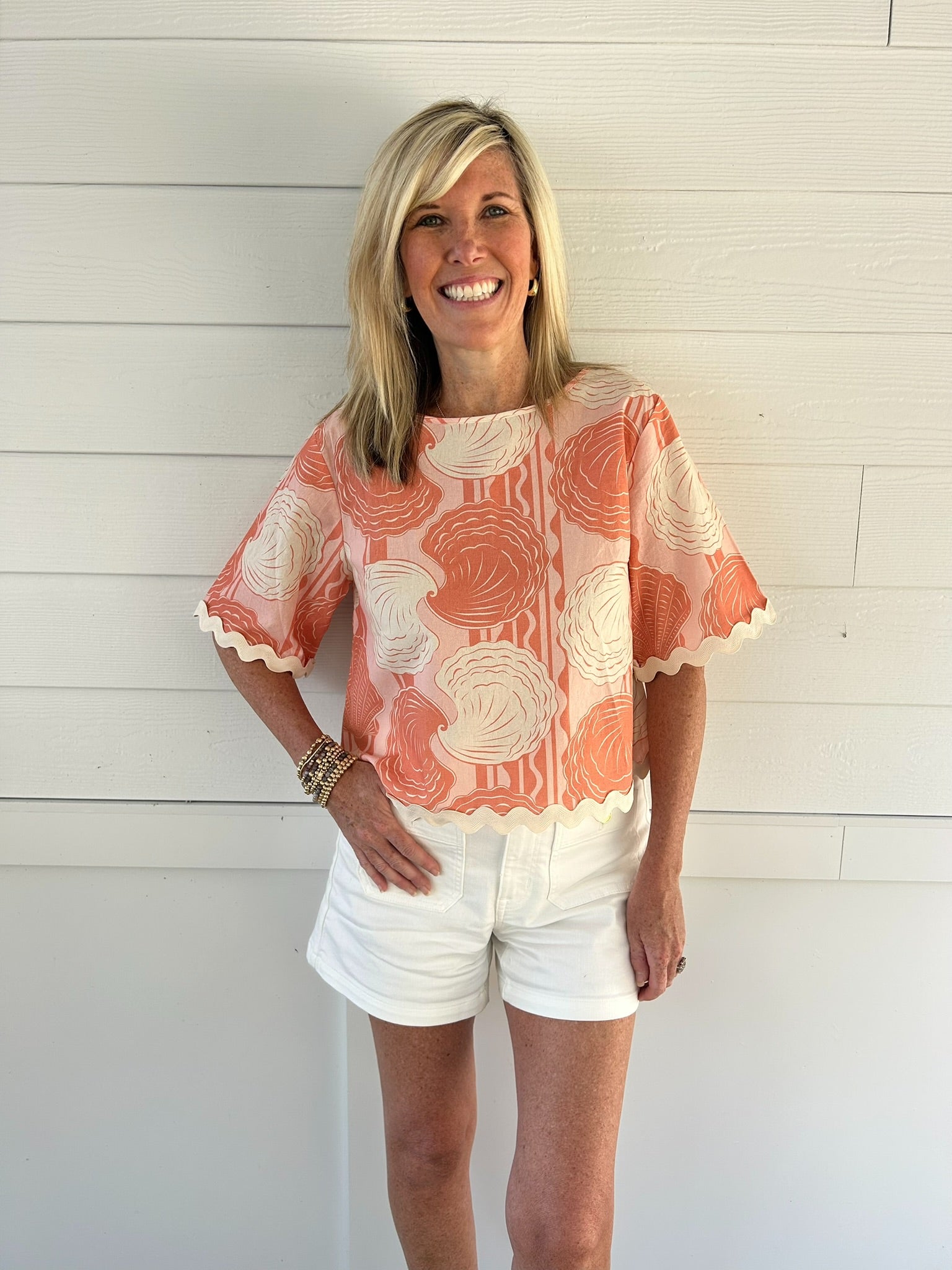 Woman wearing a coral floral blouse and white shorts against a white wooden background