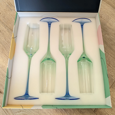Set of four green wine glasses with blue stems in a decorative box on a wooden surface.