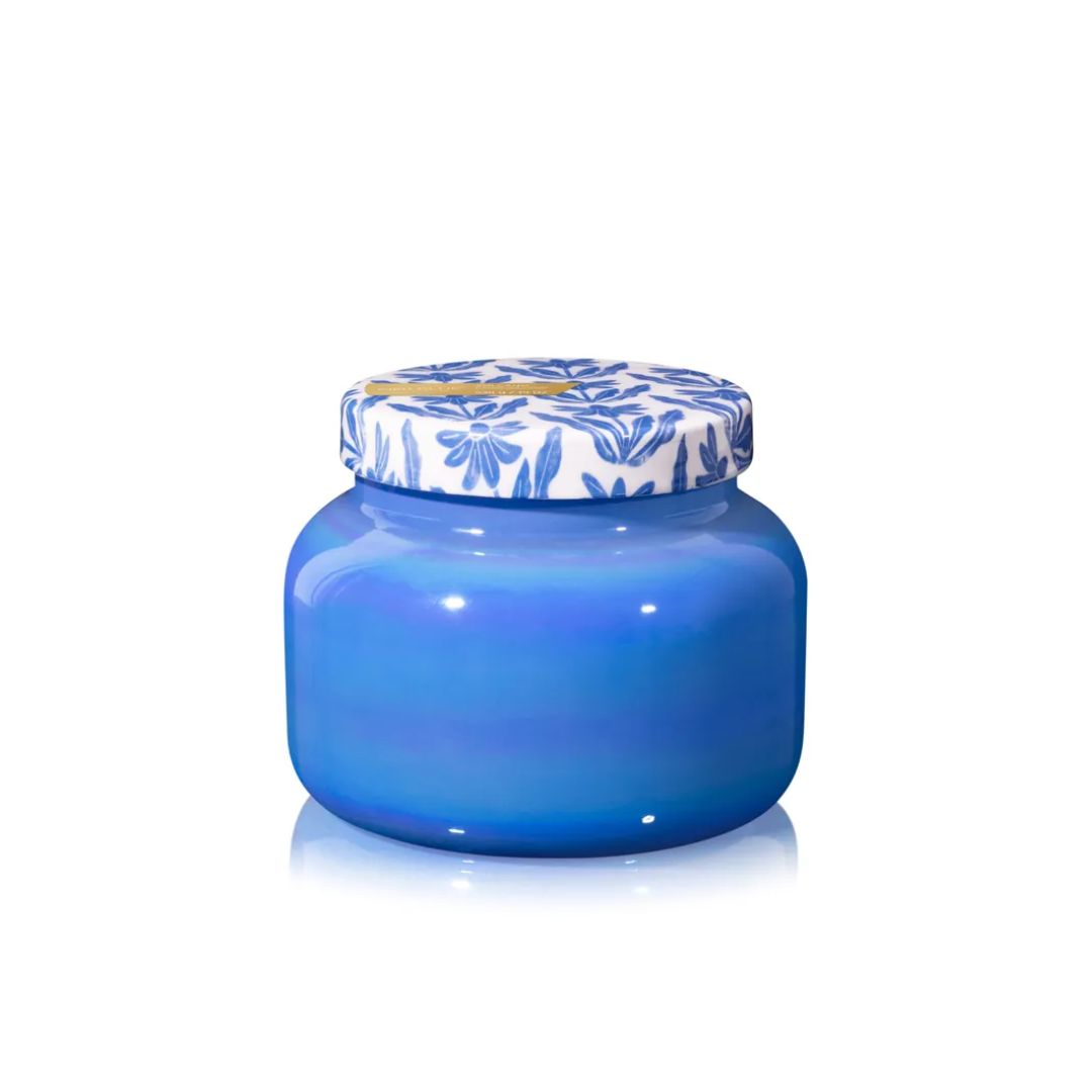 A small round glass jar with a glossy cobalt blue body and a white lid decorated with a blue floral pattern and a gold accent, set against a plain white background.