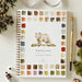 Woodland watercolor workbook featuring a painted bear and earthy watercolor swatches, styled on a light surface with a paintbrush, watercolor paint, dried flowers, pinecones and greenery.