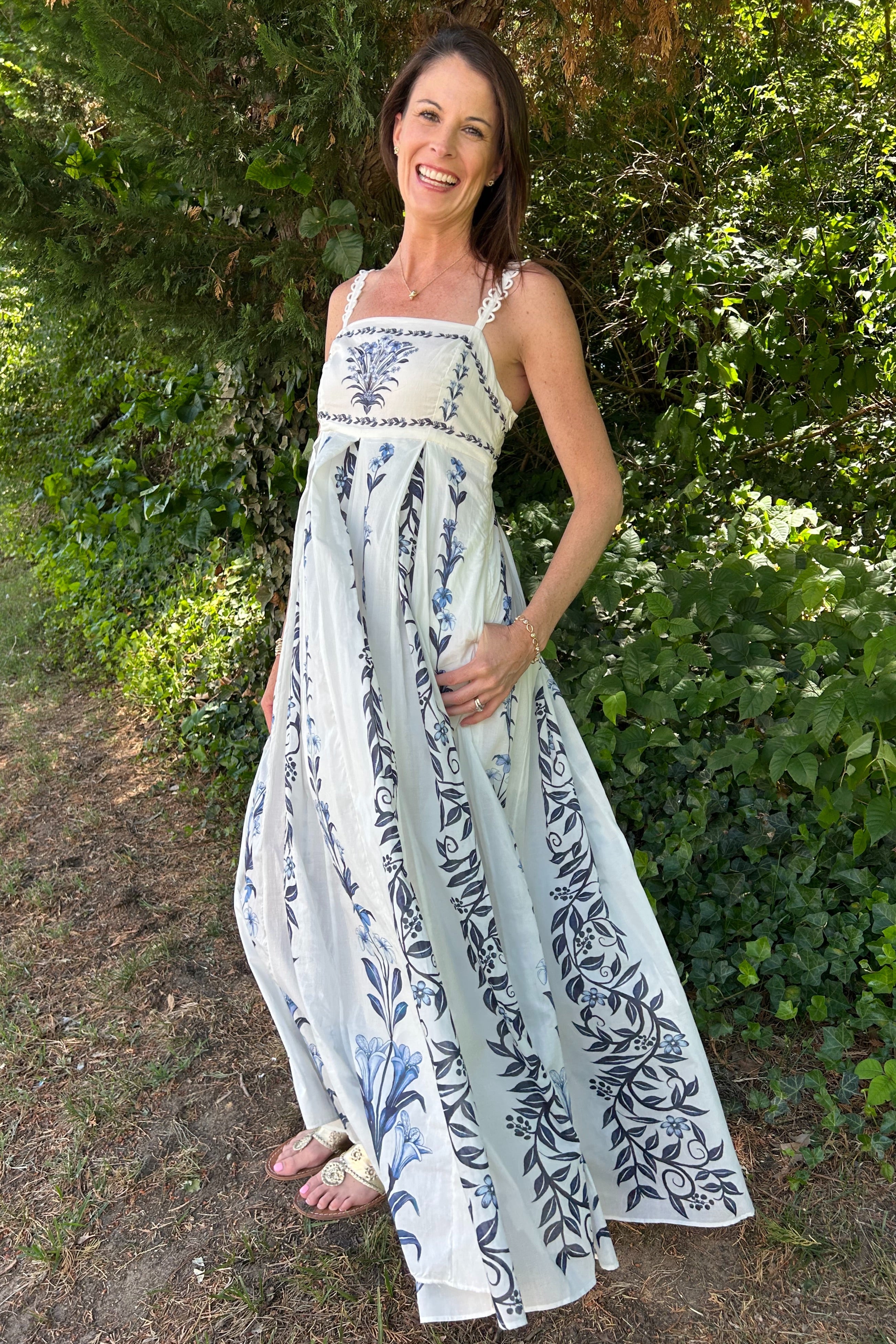 Woman wearing a long floral dress standing outdoors with greenery in the background