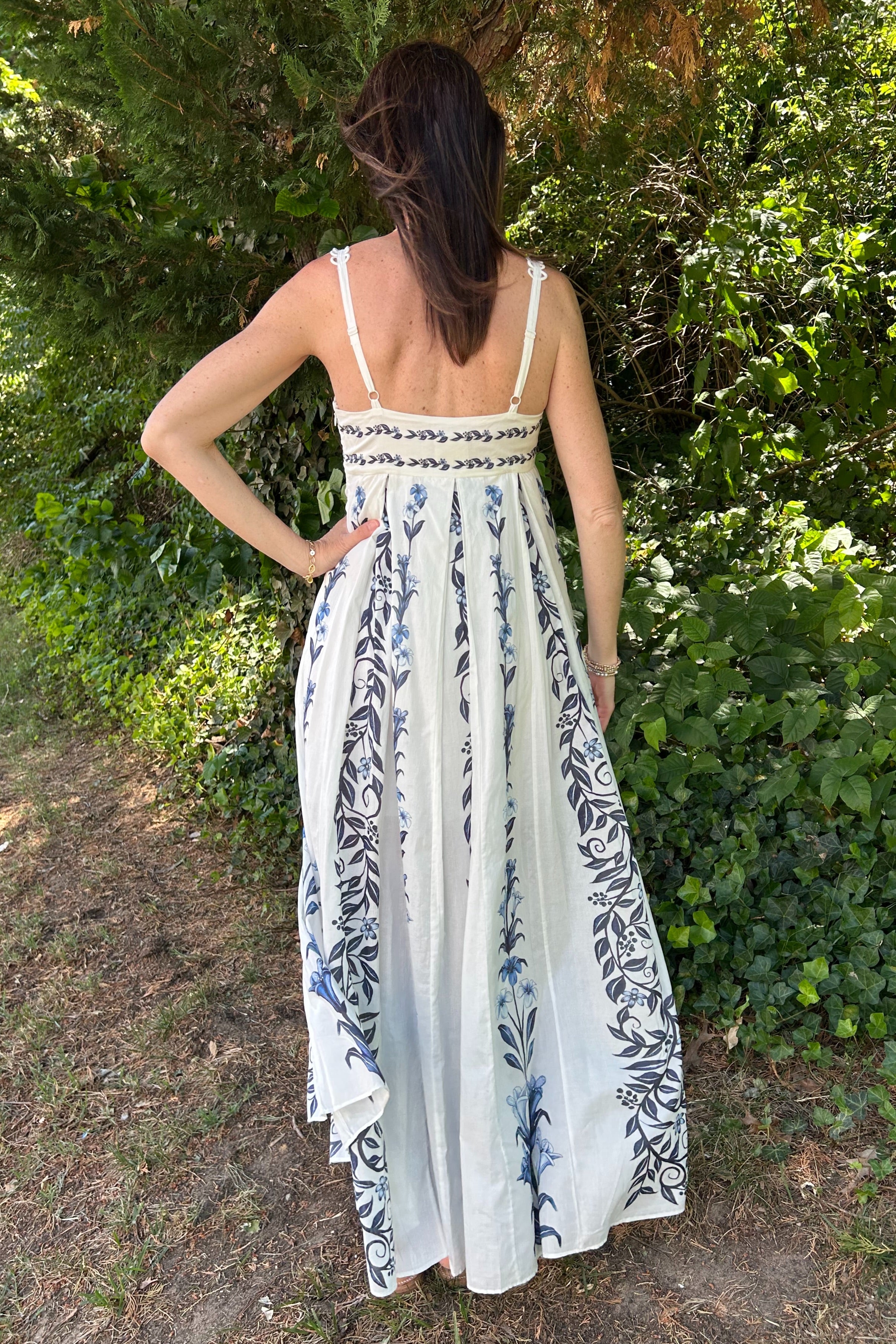 Woman wearing a white dress with blue floral pattern standing in a natural setting.