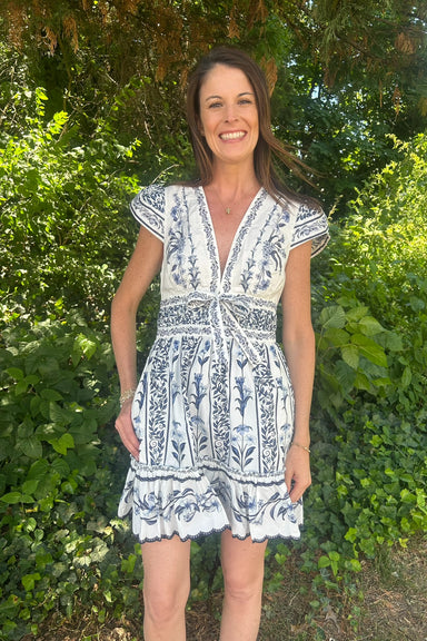Woman wearing a blue and white patterned dress standing in front of green foliage