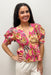 Woman wearing a vibrant pink floral top against a plain background