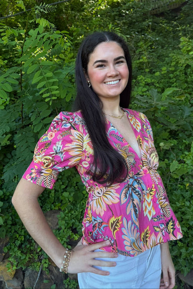 Woman wearing a colorful floral blouse standing in front of green leaves
