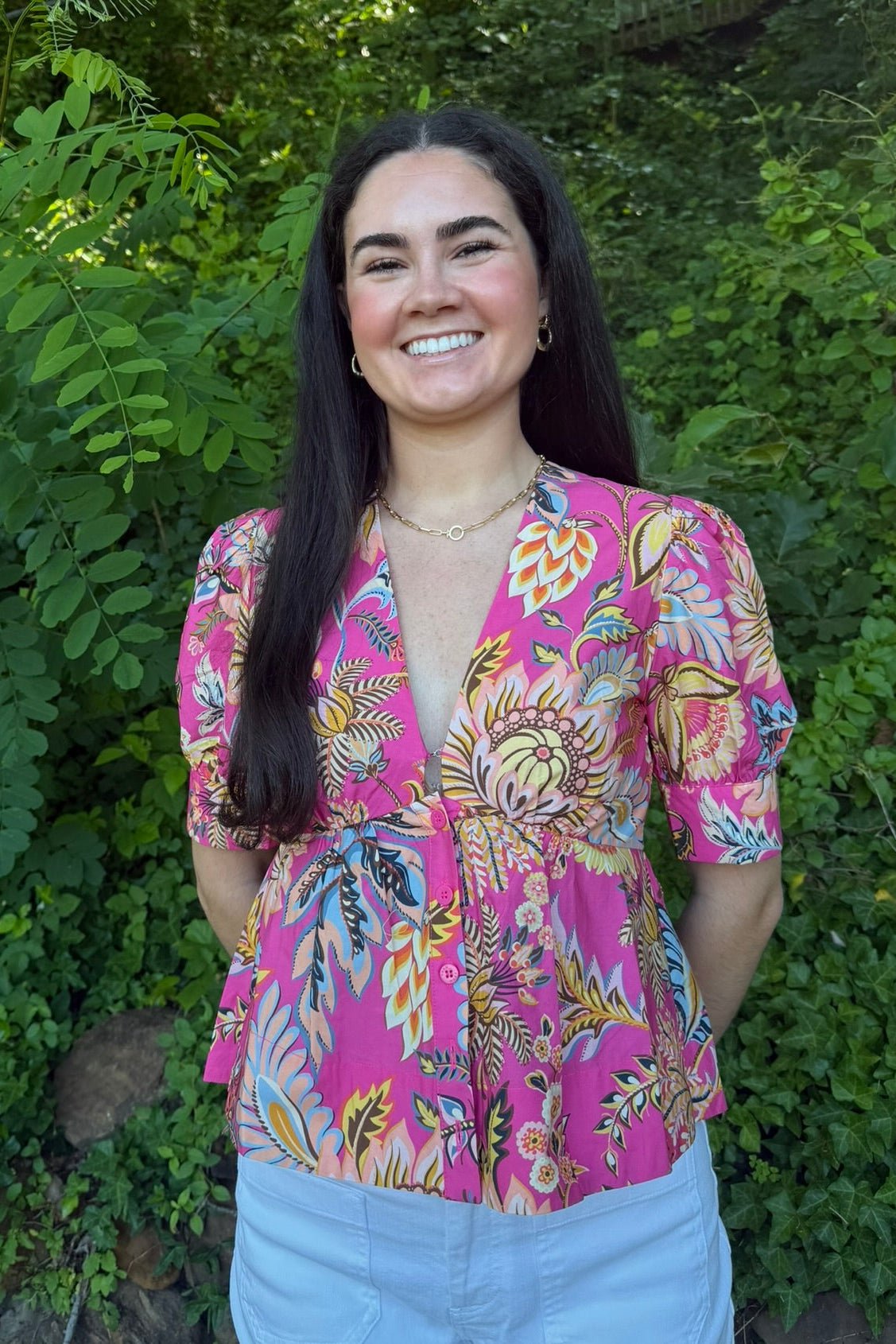 Woman wearing a colorful pink blouse with floral patterns against a green leafy background