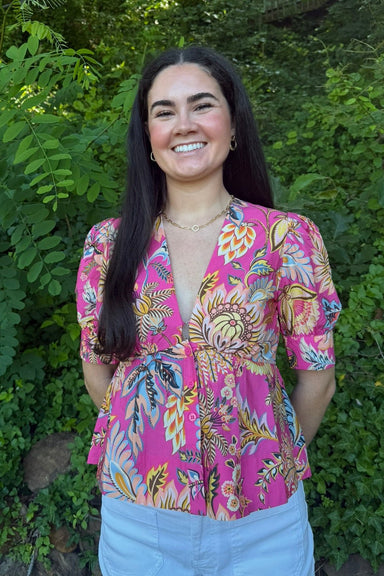 Woman wearing a colorful pink blouse with floral patterns against a green leafy background