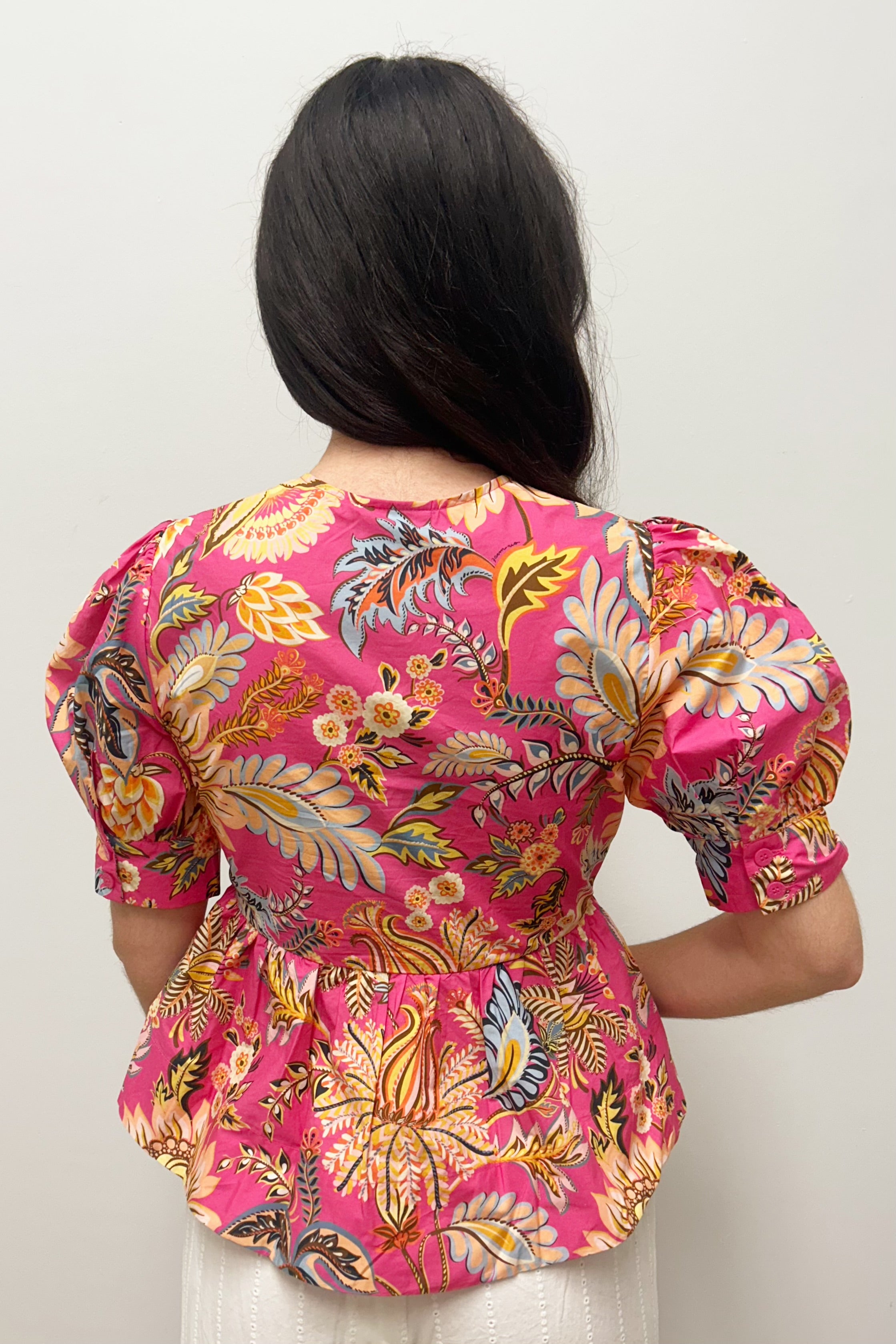 Person wearing a vibrant pink floral blouse against a plain background