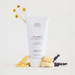 A white tube of FHF Farmhouse Fresh Organics DreamWell Magnesium Shea Butter body cream, styled with yellow flowers, soap bars, and lavender on a clean white background.