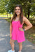 A woman posing outdoors on a paved path in a park, wearing a bright pink sleeveless tankini-style mini dress with a front pocket.